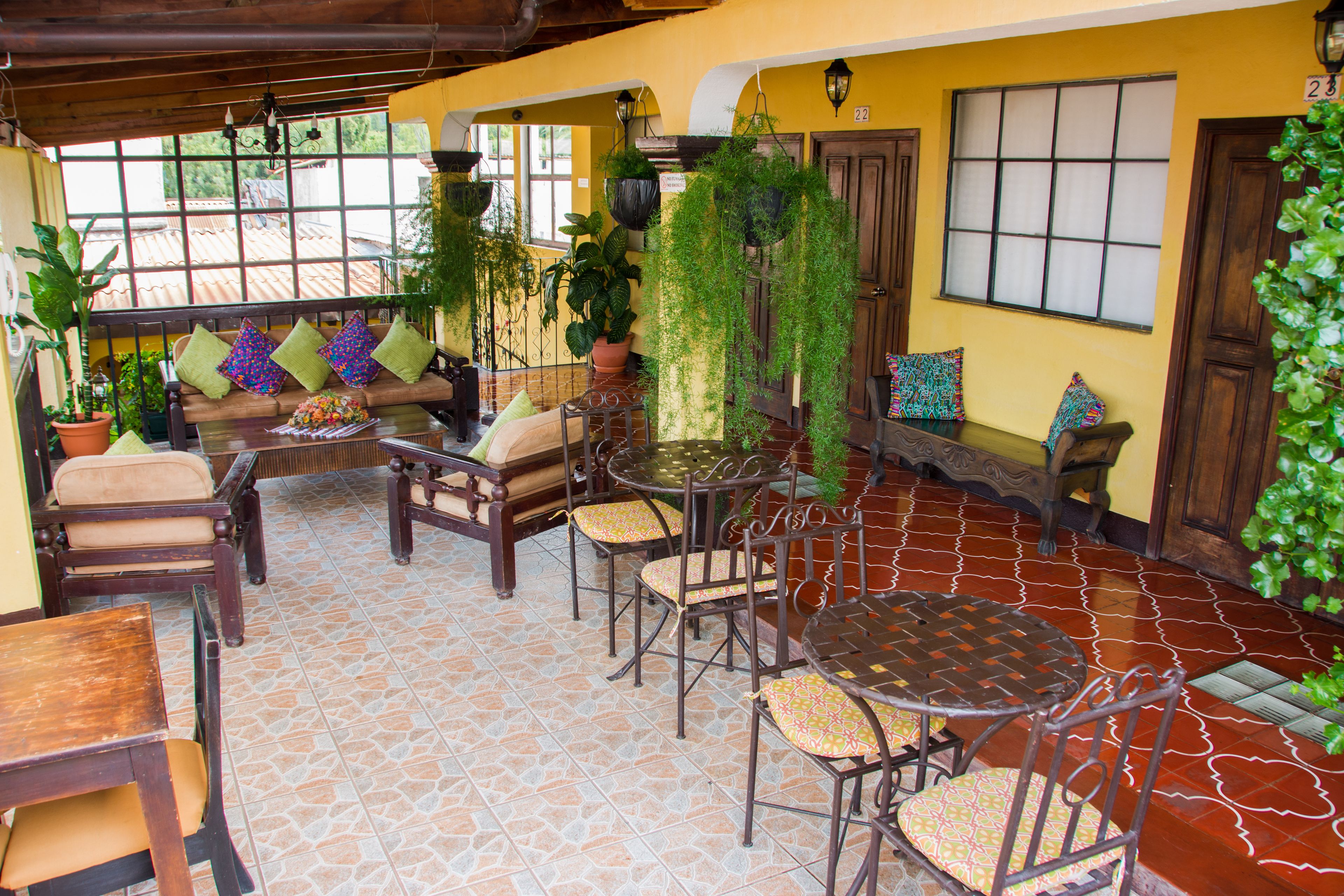 Un área de patio acogedora con un banco de madera, una mesa redonda y sillas, rodeada de plantas en macetas y un suelo de baldosas.