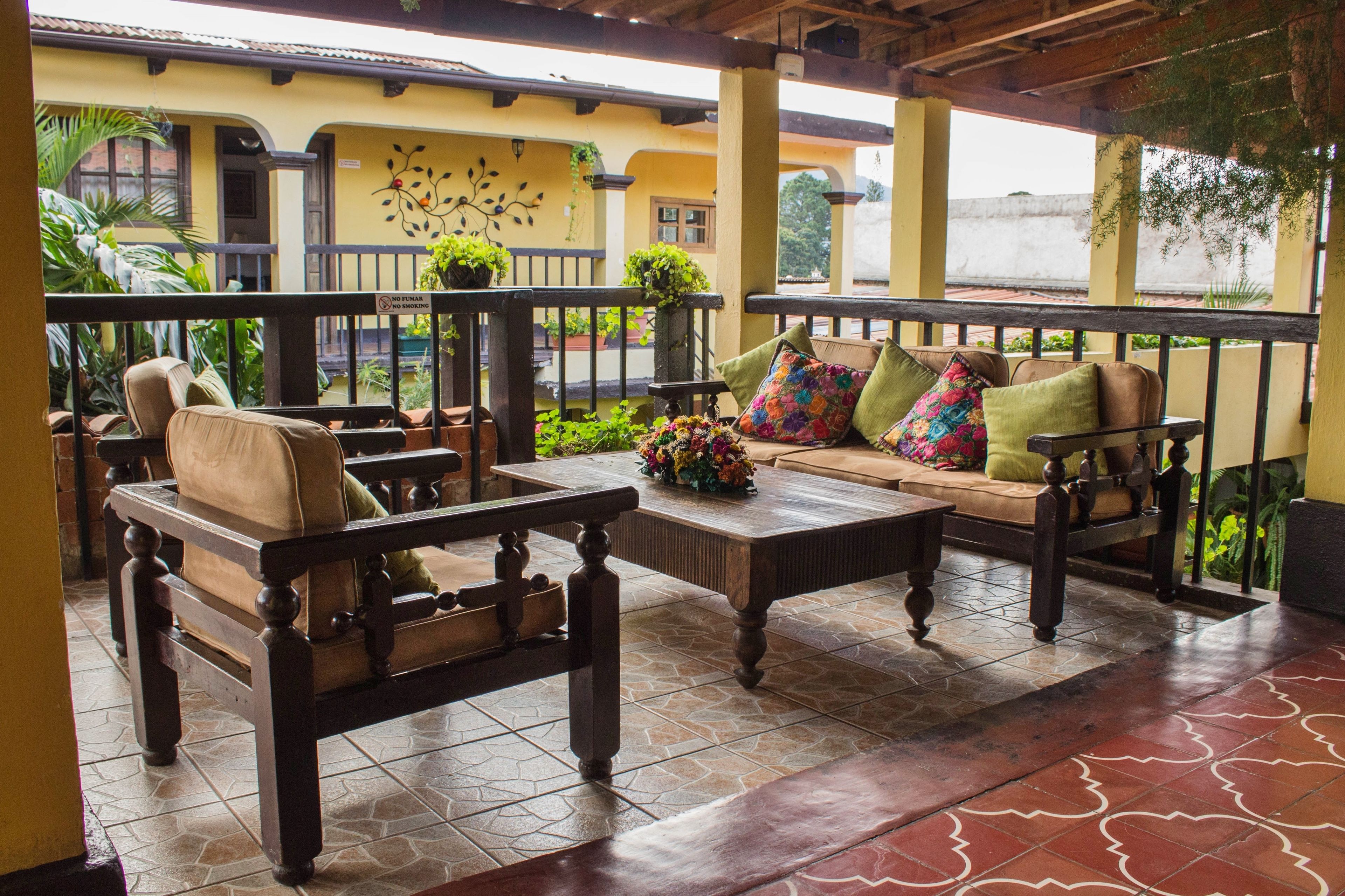 Un patio con mobiliario de madera, piso de baldosas y plantas en macetas.