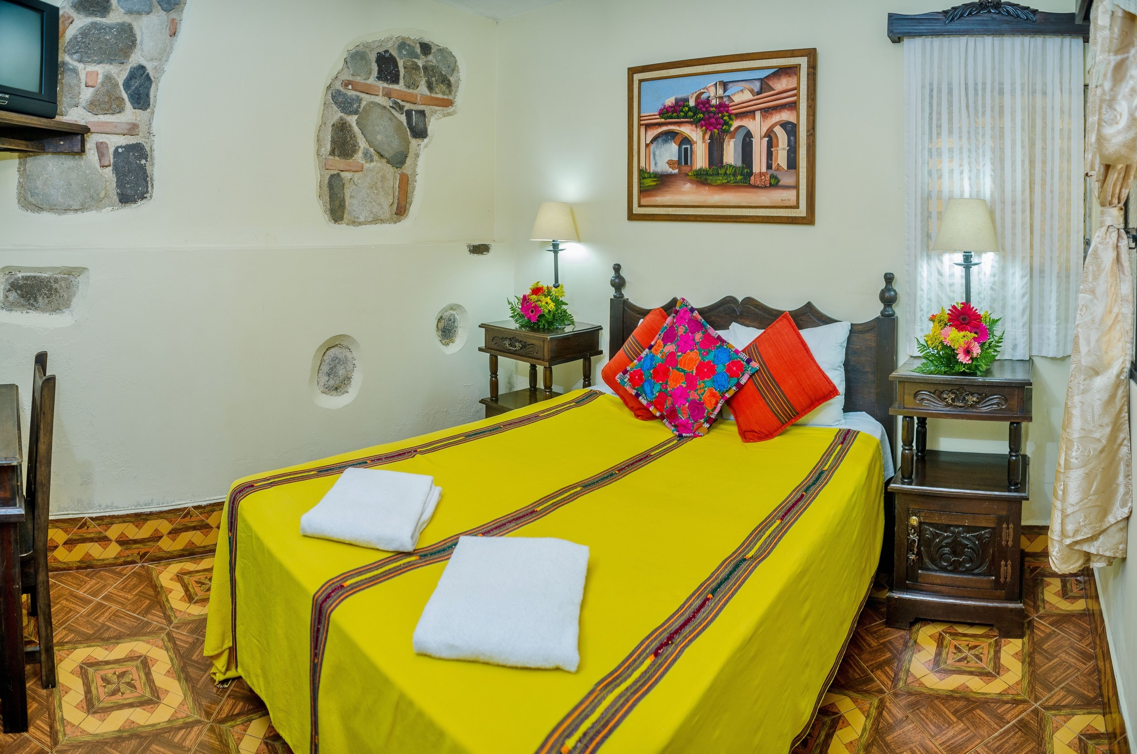 A hotel room with a large bed, two bedside tables with lamps, a stone wall, and a painting on the wall.