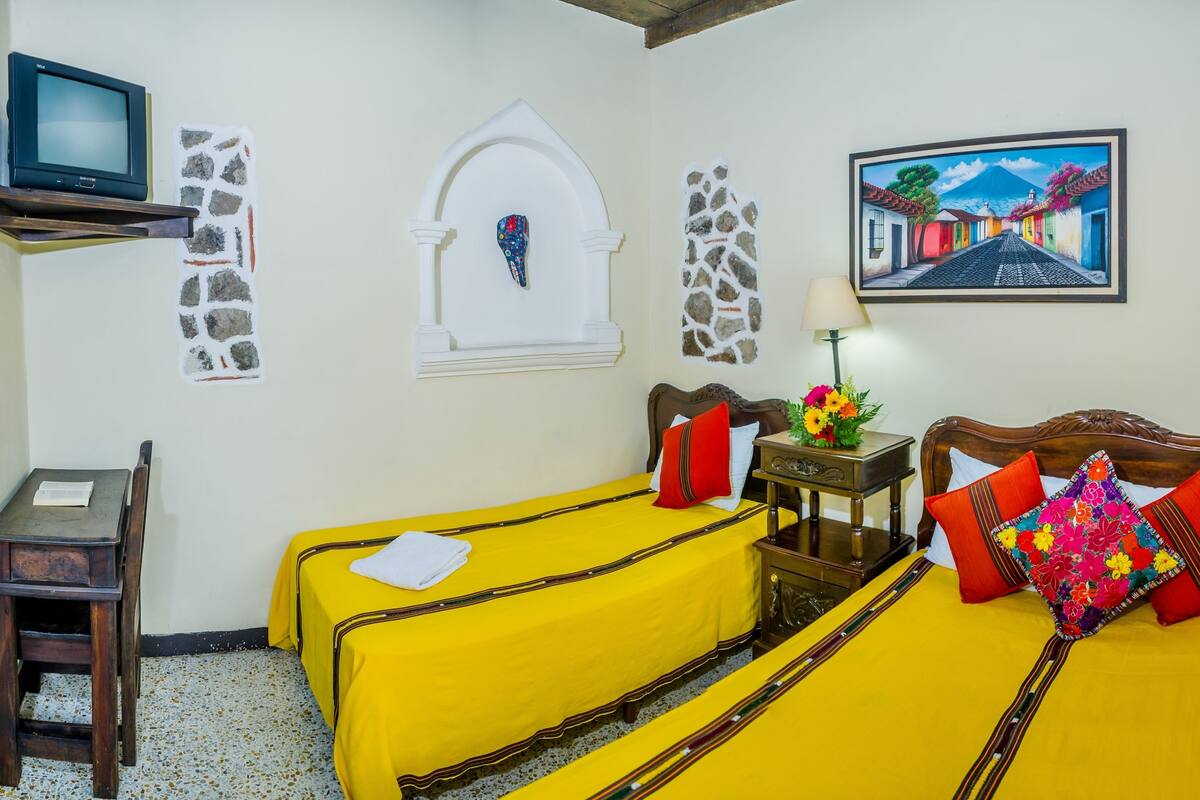 Una habitación con dos camas, un escritorio, un televisor y un cuadro en la pared.