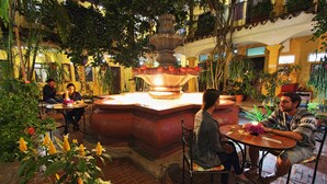 Un patio con una fuente central, rodeado de mesas y sillas, y abundante vegetación.