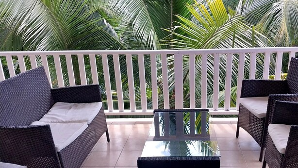 Un balcon agrémenté de meubles en osier, d’une table en verre et d’une balustrade blanche.