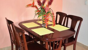 Une table de salle à manger en bois, quatre chaises, un vase avec des fleurs et des sets de table jaunes.