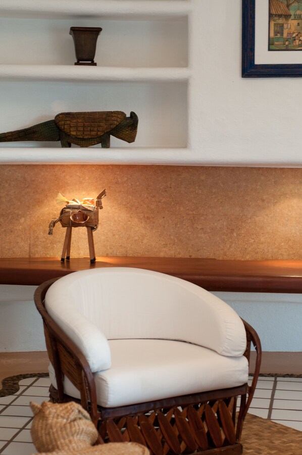Una habitación con una silla blanca acolchada, un banco de madera y una estantería con un objeto decorativo.