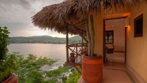 Une pièce avec vue sur un lac, une structure à toit de chaume et un cactus en pot.