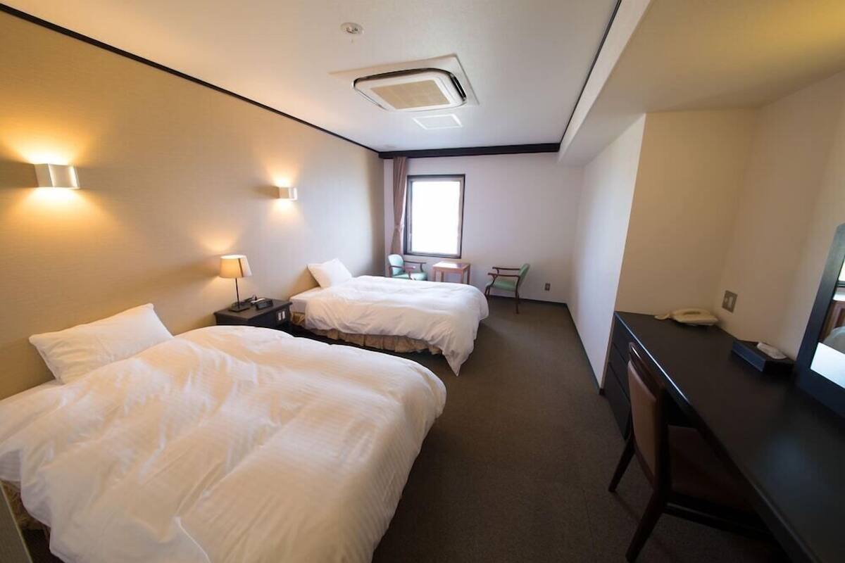 Une chambre d’hôtel avec deux lits, un bureau, une chaise, une petite table et une fenêtre.