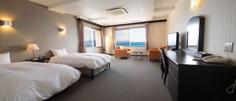 A hotel room with two beds, a desk with a telephone, a television, and a view of the sea.