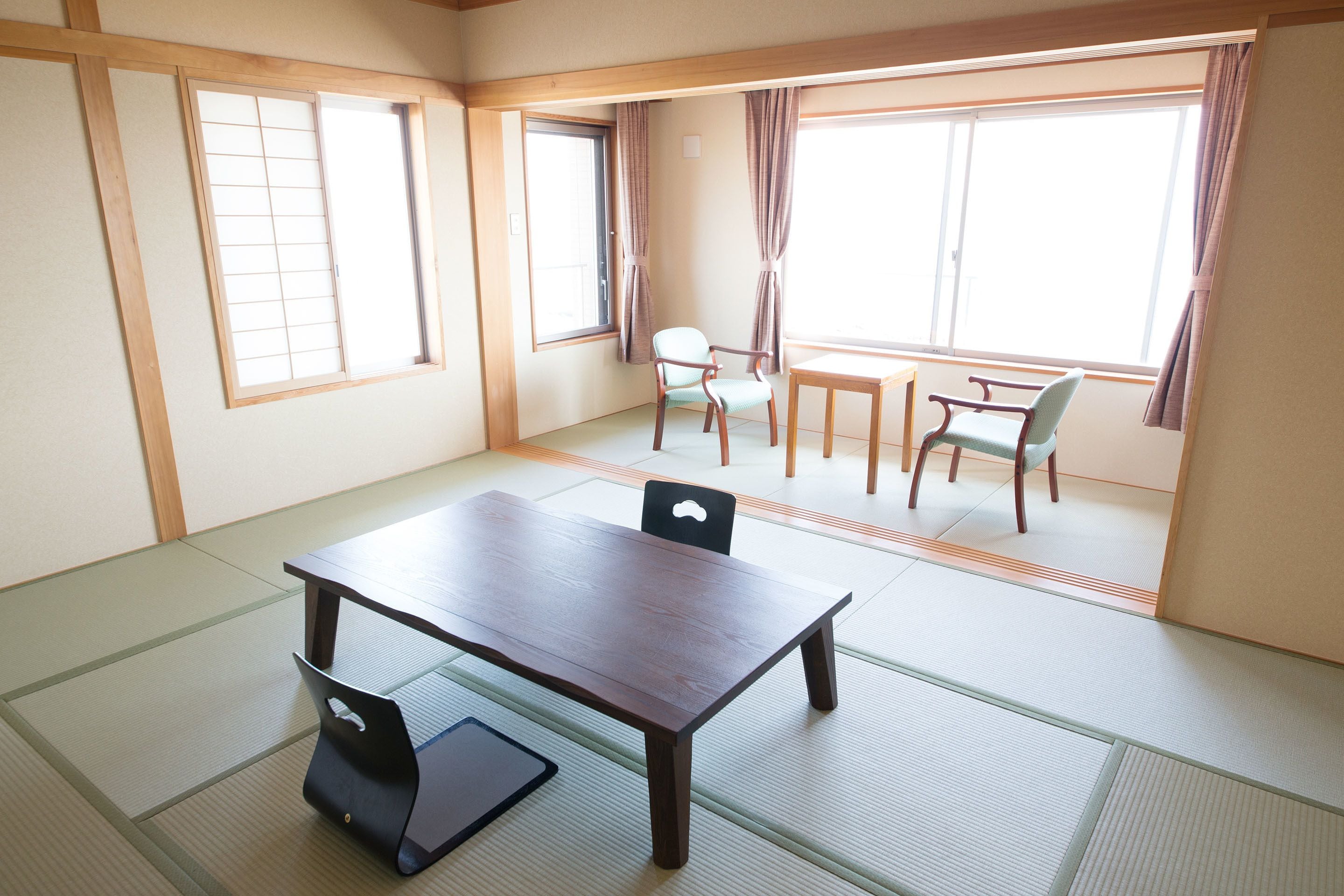 A traditional Japanese room with tatami flooring, a low table, and two chairs.
