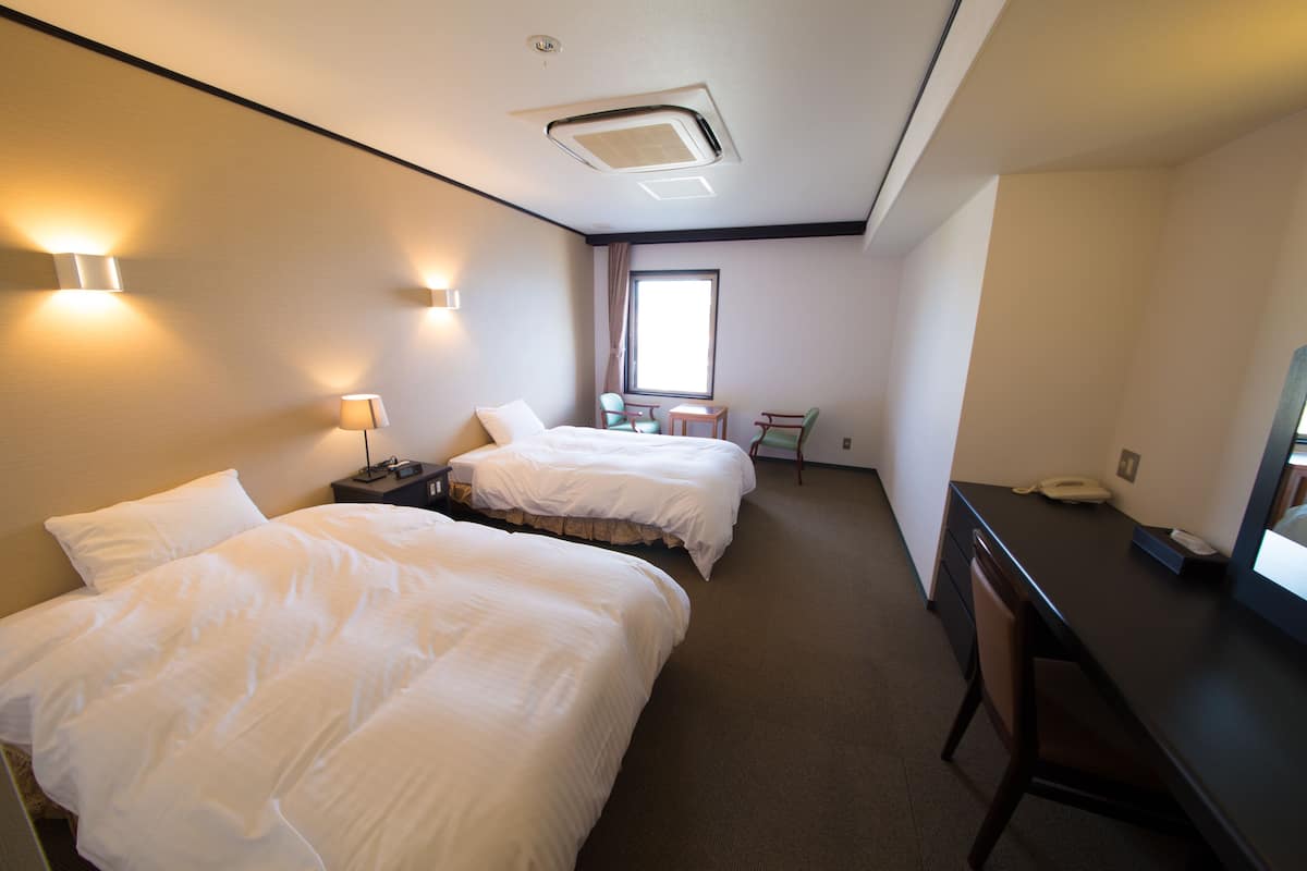 A hotel room with two beds, a desk, a chair, a small table, and a window.
