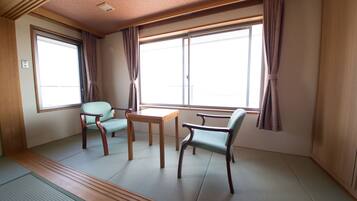 A room with tatami flooring, a wooden table, two chairs, and large windows with curtains.