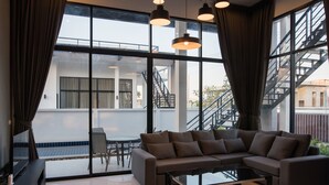 Un salon moderne avec un canapé d’angle, une table basse en verre et de grandes fenêtres dotées de rideaux.