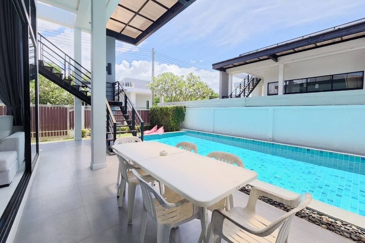 Un espacio exterior techado con piscina, una mesa con sillas y una escalera que lleva a un nivel superior.