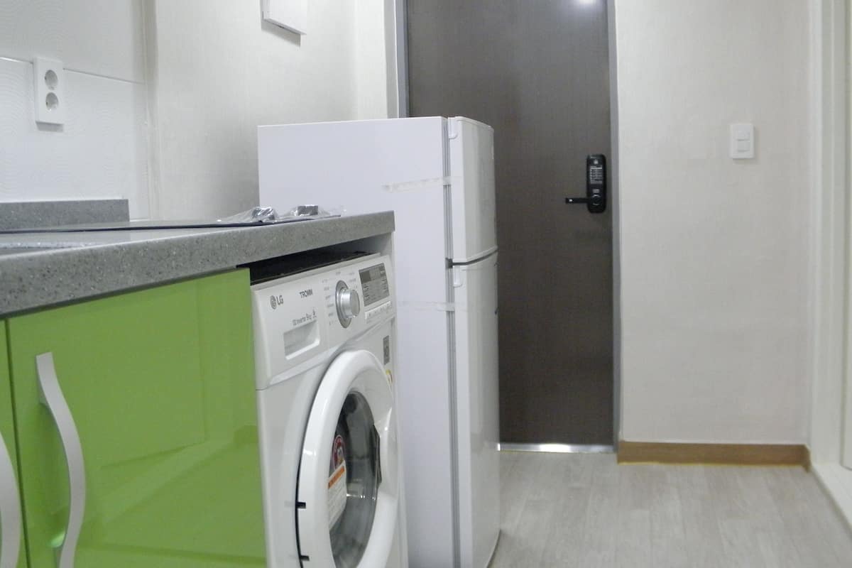 A compact kitchen with a washing machine, a refrigerator, and a microwave.