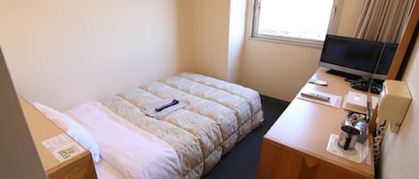 A hotel room with a bed, a desk with a computer, a TV, and a window with curtains.