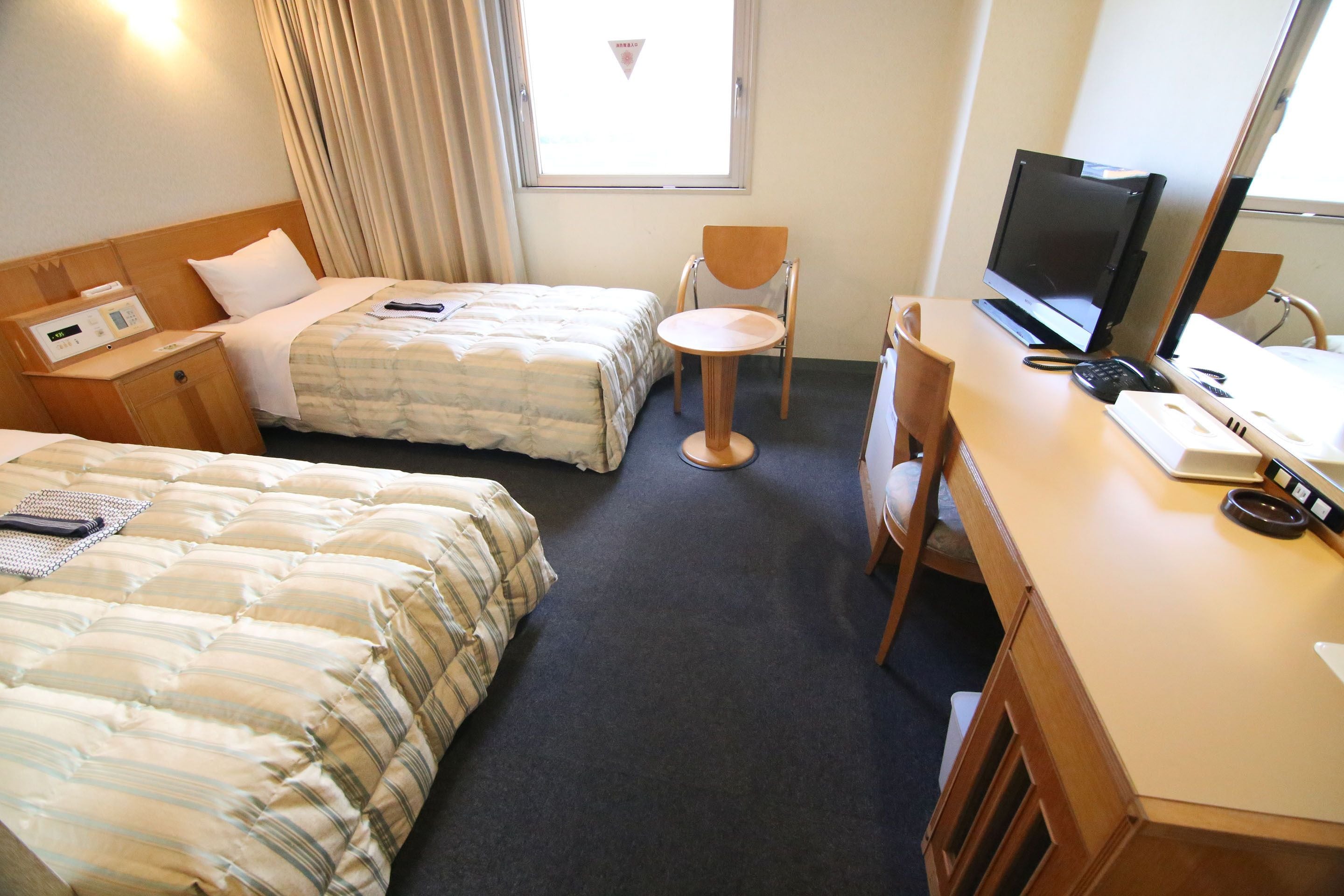 Habitación de hotel con dos camas, un escritorio con computadora, una silla y un ventanal con cortinas.