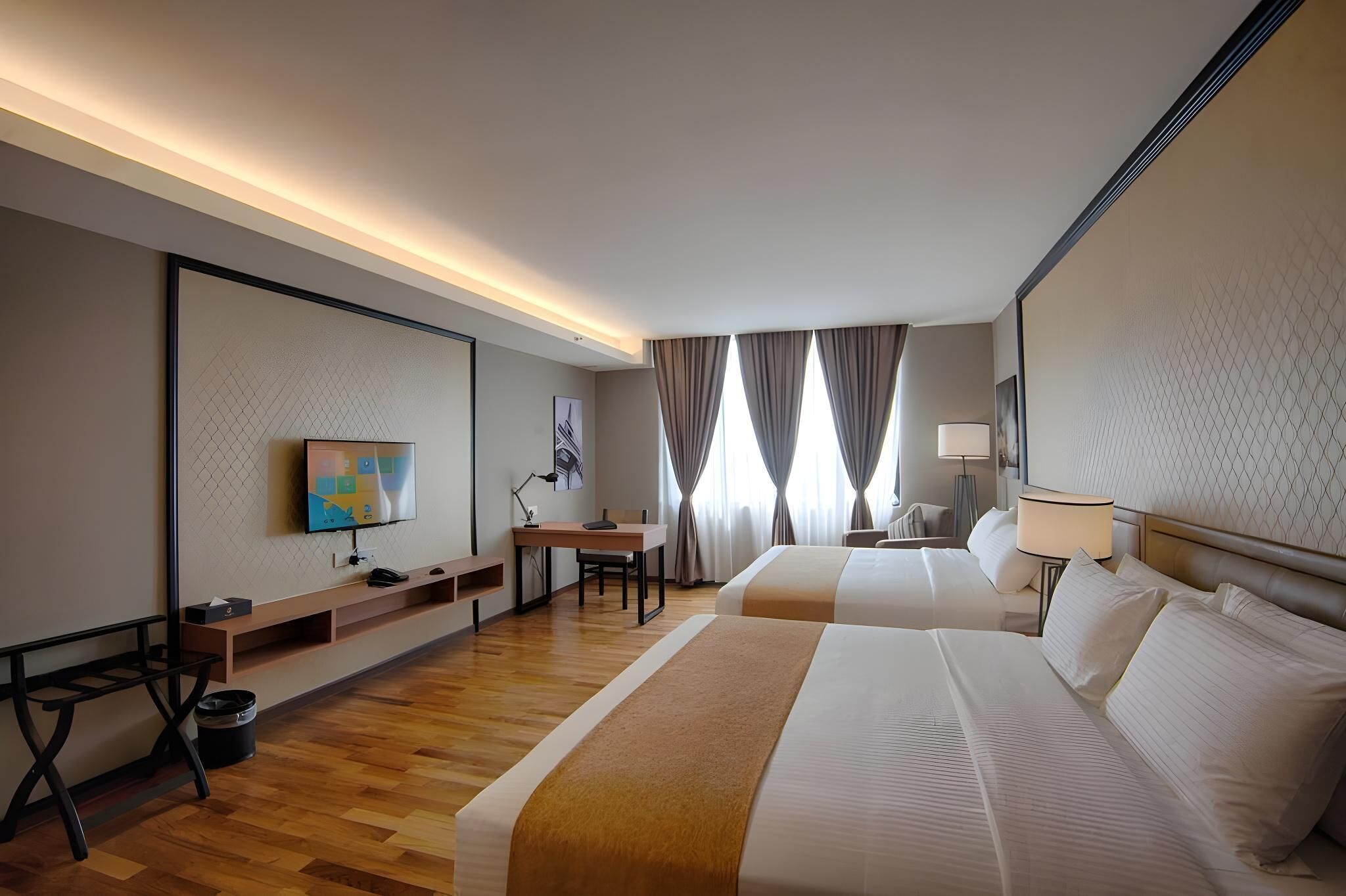 A hotel room with two beds, a desk, a TV, and a window with curtains.
