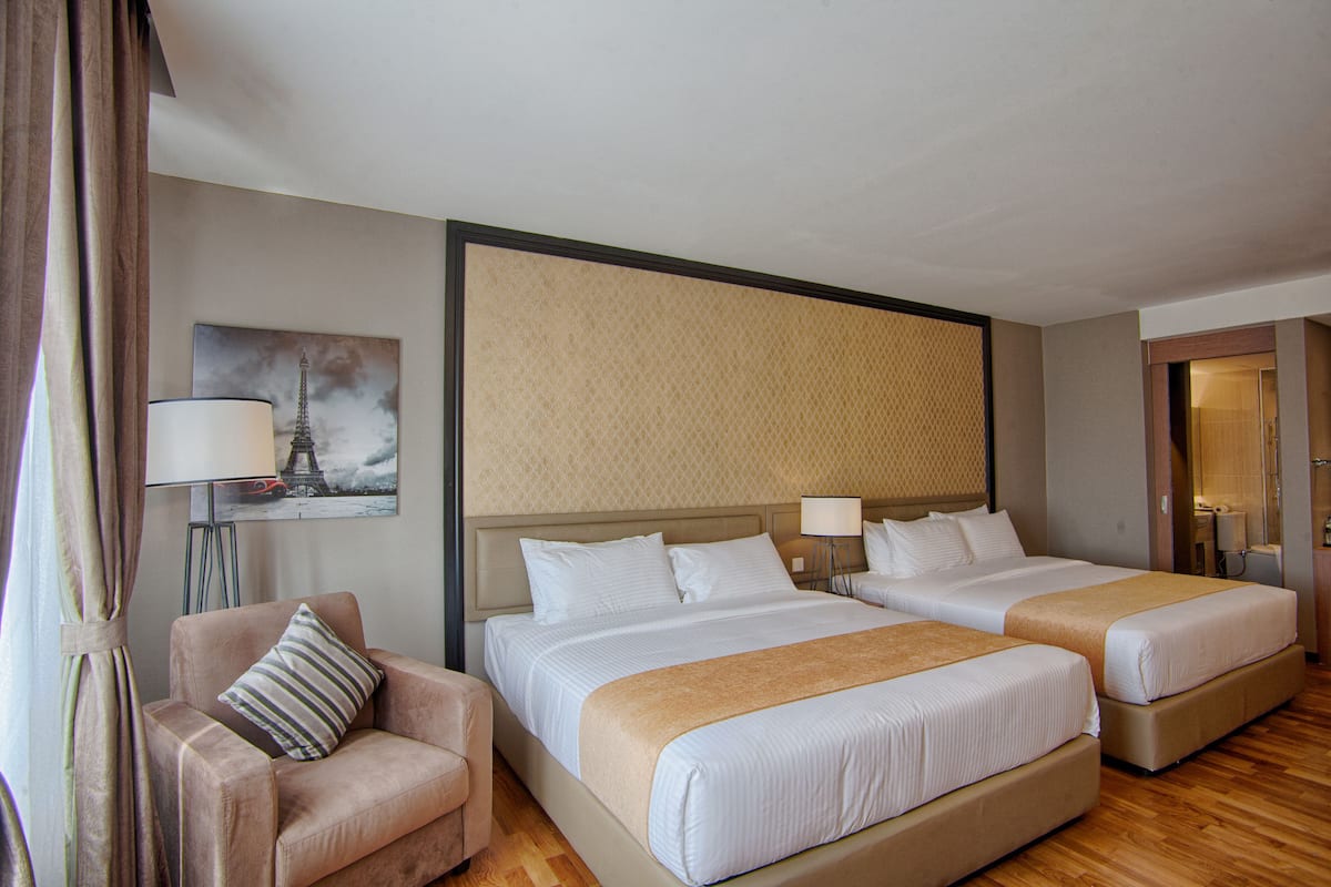 A hotel room with two beds, a sofa, a lamp, and a painting of the Eiffel Tower.