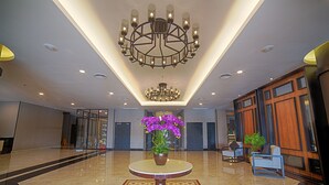 Um hall espaçoso com uma mesa redonda central, um grande candelabro e um vaso com flores roxas.