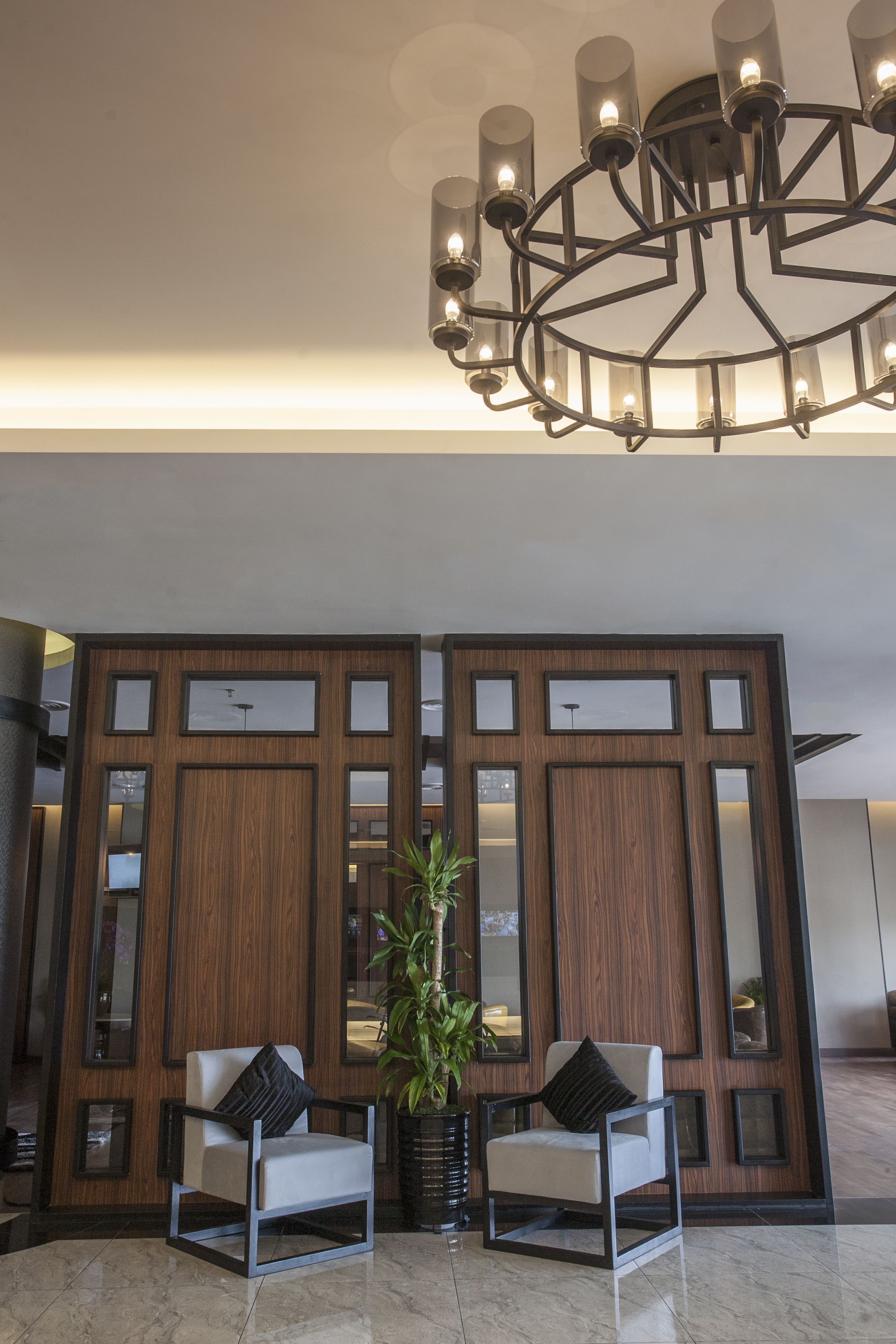 Un hall d’entrée avec deux fauteuils blancs, une grande plante en pot et un lustre moderne.