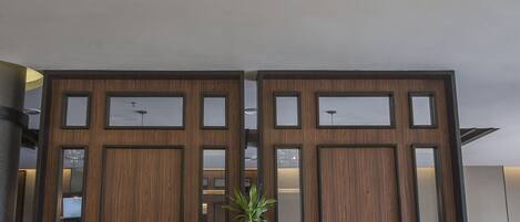 Un hall d’entrée avec deux fauteuils blancs, une grande plante en pot et un lustre moderne.