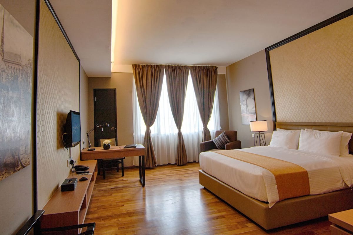 A hotel room with a bed, desk, chair, TV, and curtains.