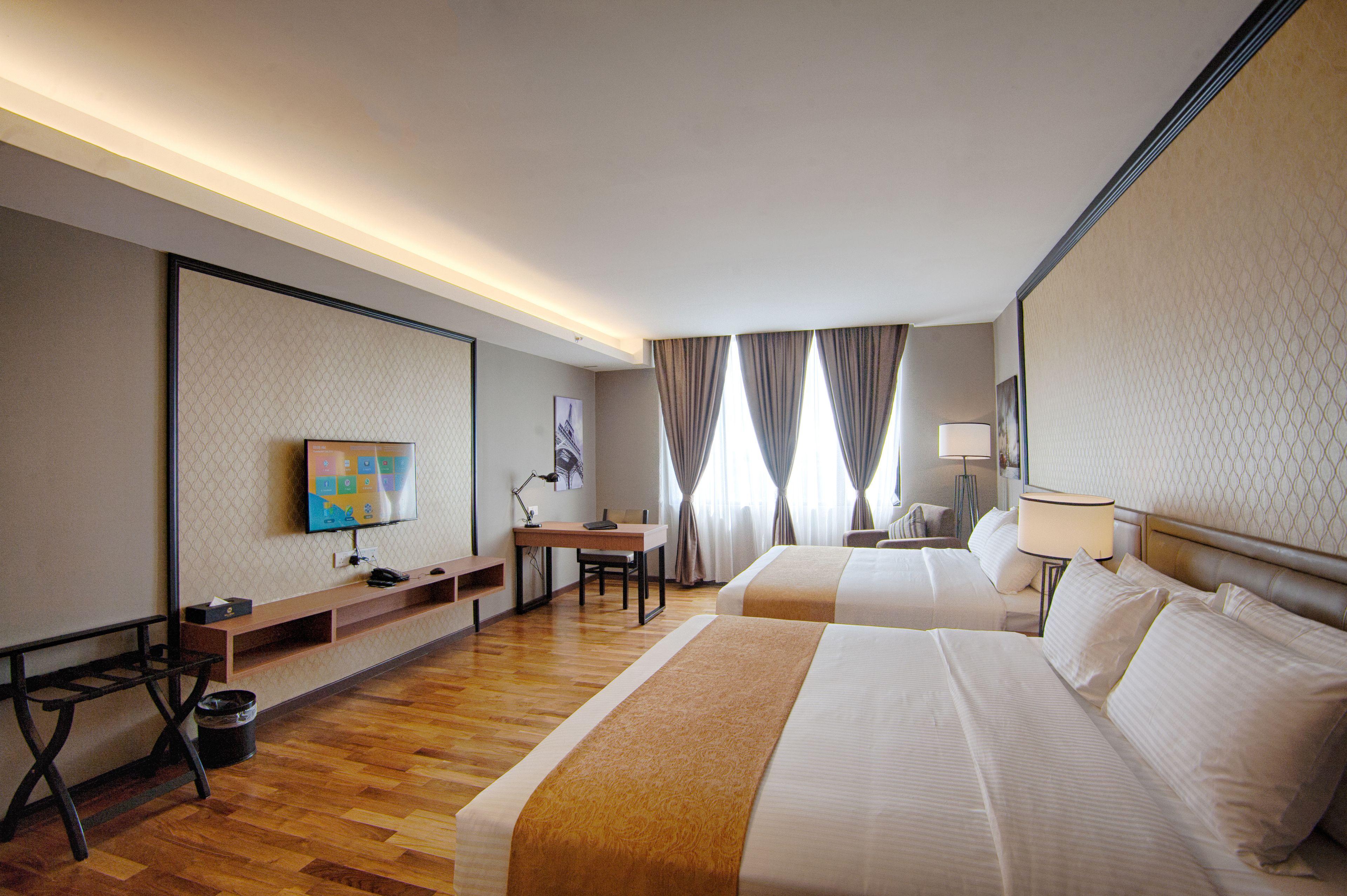 A hotel room with two beds, a desk, a chair, a TV, and a lamp.