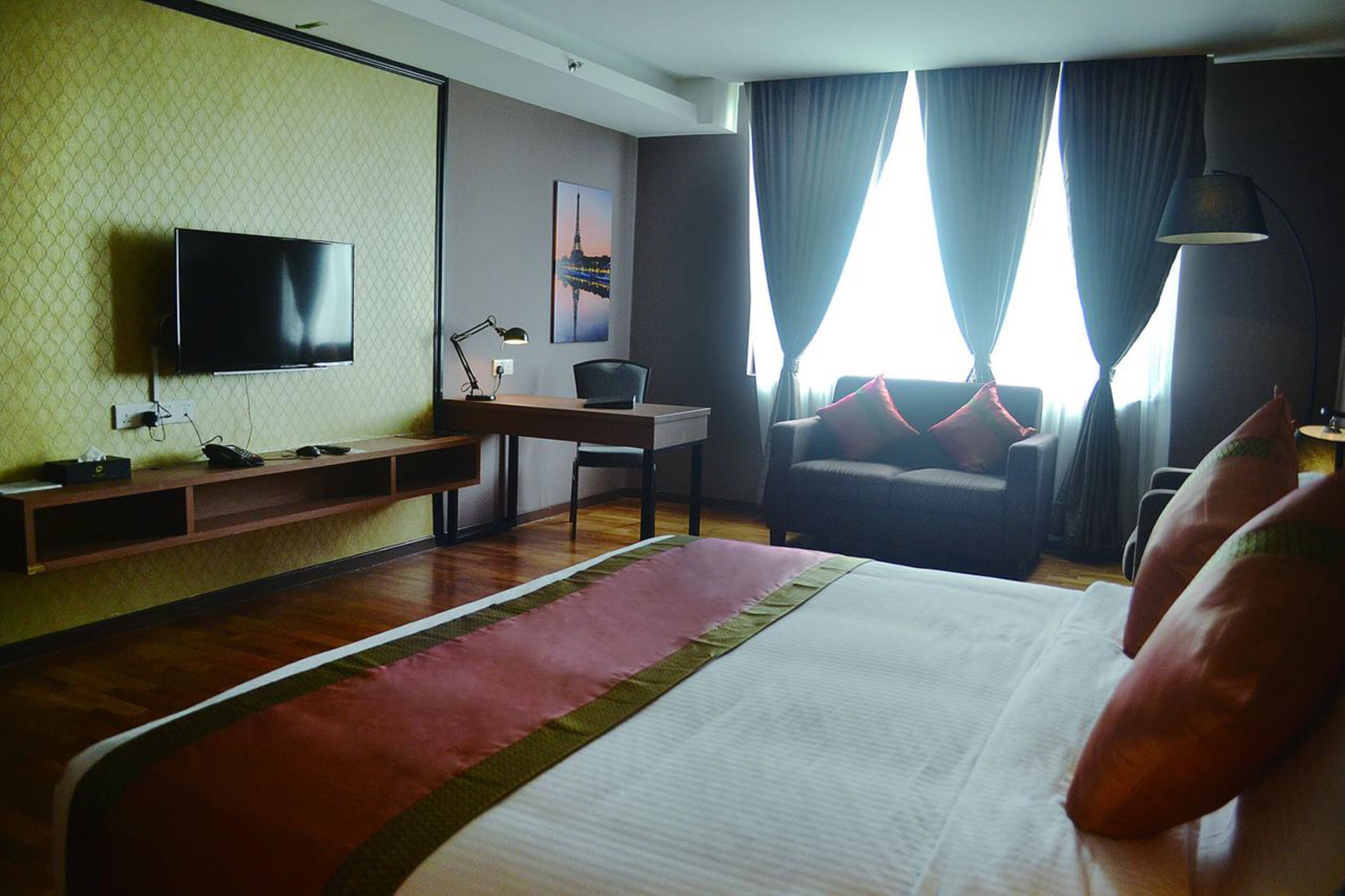 A hotel room with a bed, a desk, a chair, a TV, and a window with curtains.