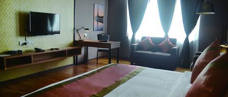 A hotel room with a bed, a desk, a chair, a TV, and a window with curtains.
