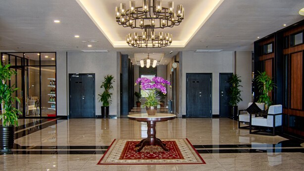 Um hall amplo com um grande candelabro, uma mesa central com um vaso de flores e plantas em vasos.