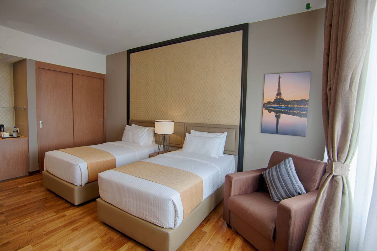 A hotel room with two beds, a sofa, a lamp, and a picture of the Eiffel Tower.
