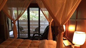 A hotel room with a bed, a nightstand, a lamp, and a view of an outdoor seating area with chairs and a table. - Hotel Wacha Wacha - Adults Only (Kyoto)
