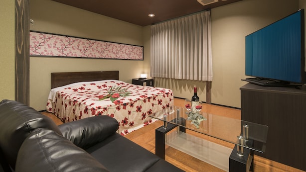 A hotel room with a bed, a sofa, a glass coffee table, a television, and a window with curtains. - Hotel Wacha Wacha - Adults Only (Kyoto)