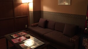 A dimly lit room with a brown sofa, a small table with magazines and a cup, and a wall with a framed artwork. - Hotel Wacha Wacha - Adults Only (Kyoto)
