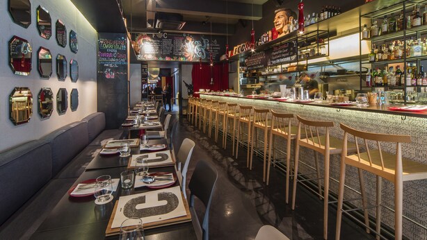 Zona de bar amb una barra llarga, diverses cadires i una varietat de botelles a les prestatgeries.