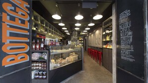 Interior de restaurant amb una vitrina expositora, prestatges plens de botelles i un quadre negre amb un menú que ofereix pizzes i cerveses.