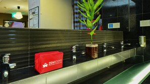 A hotel reception area with a modern design, including a reception desk, a plant, and a red bag labeled "ZENROOMS". - River City Inn - Hostel (Singapore)