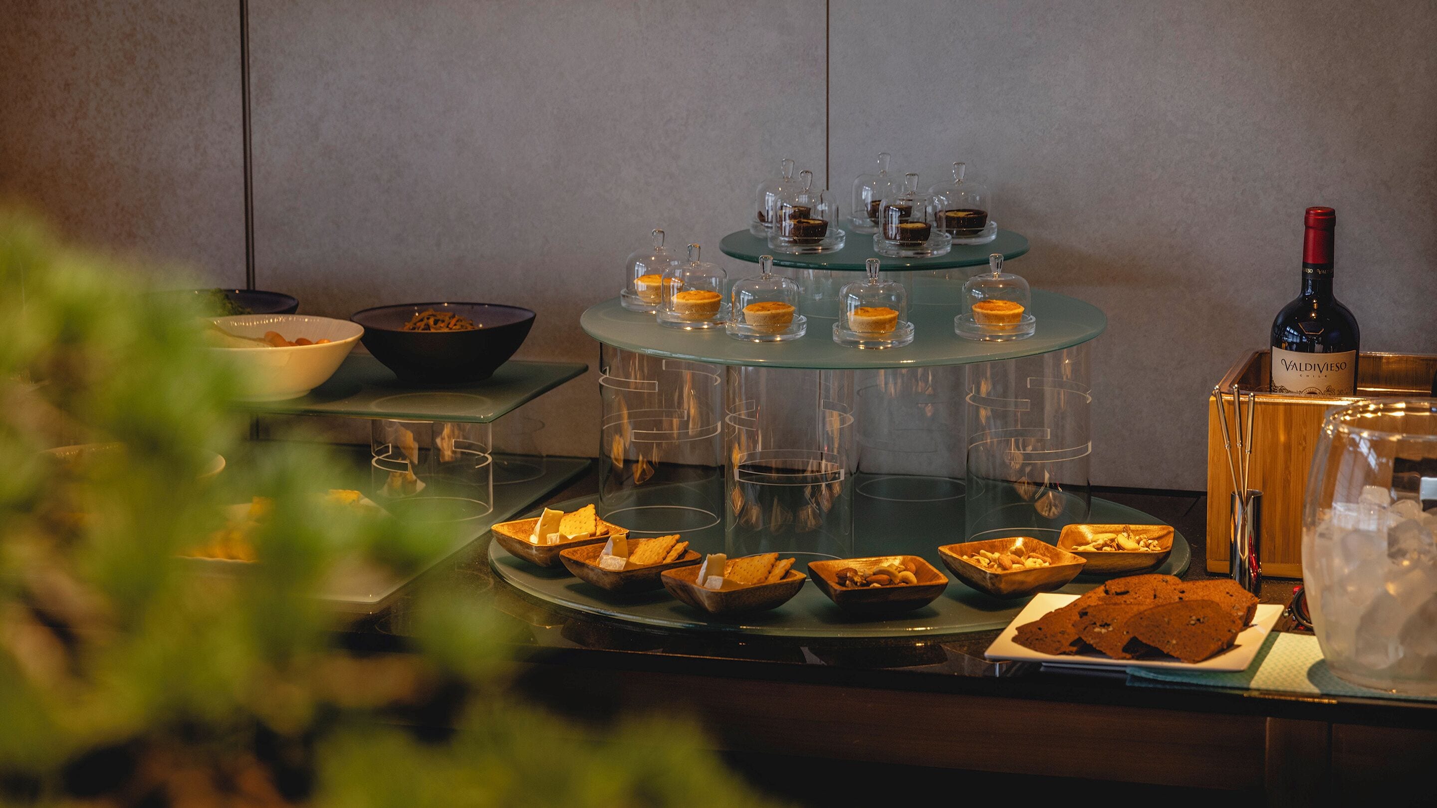 A buffet setup with various food items and a bottle of wine on a glass table.