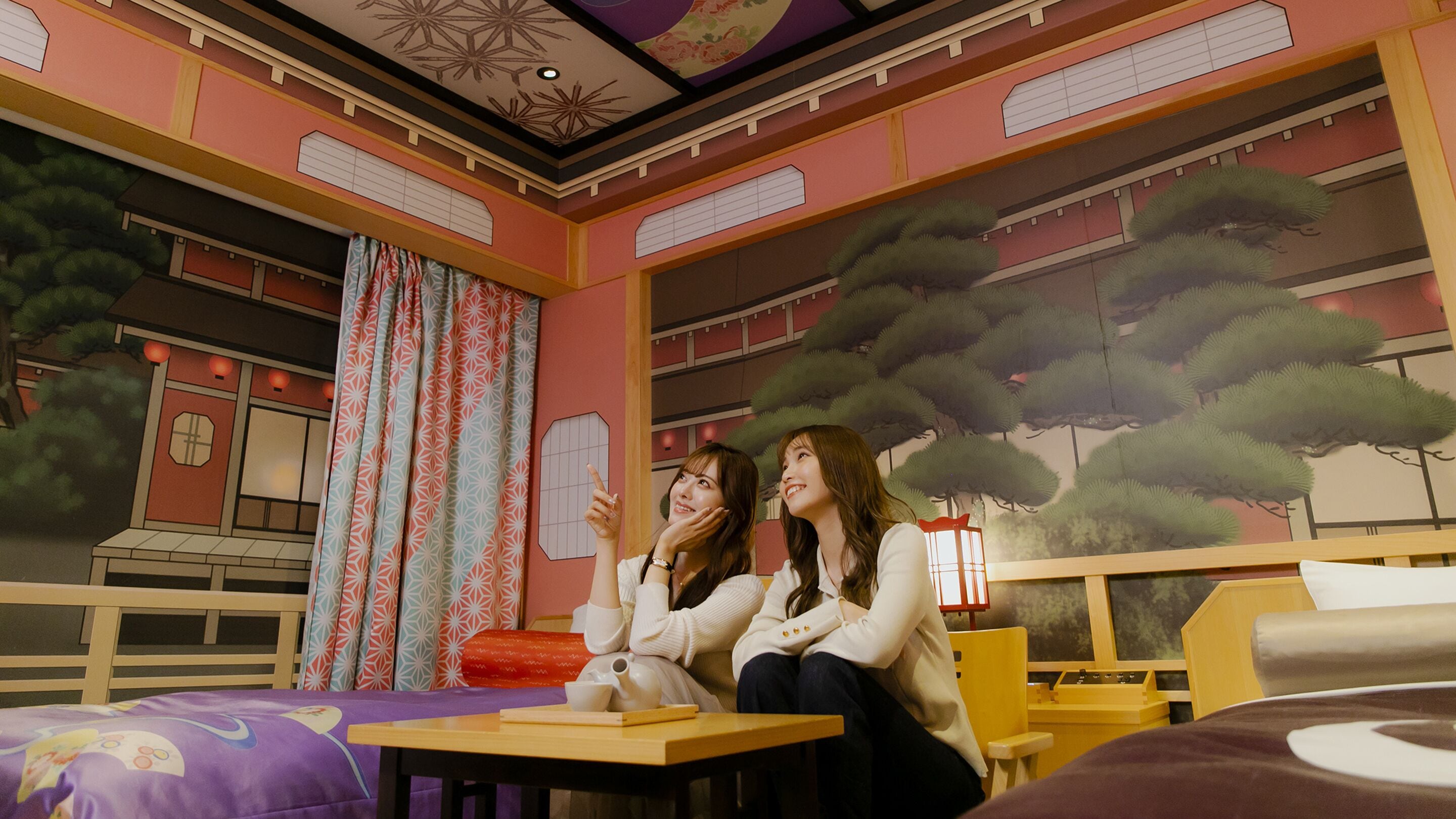 A room with a bed, a table, and a mural of a traditional building.