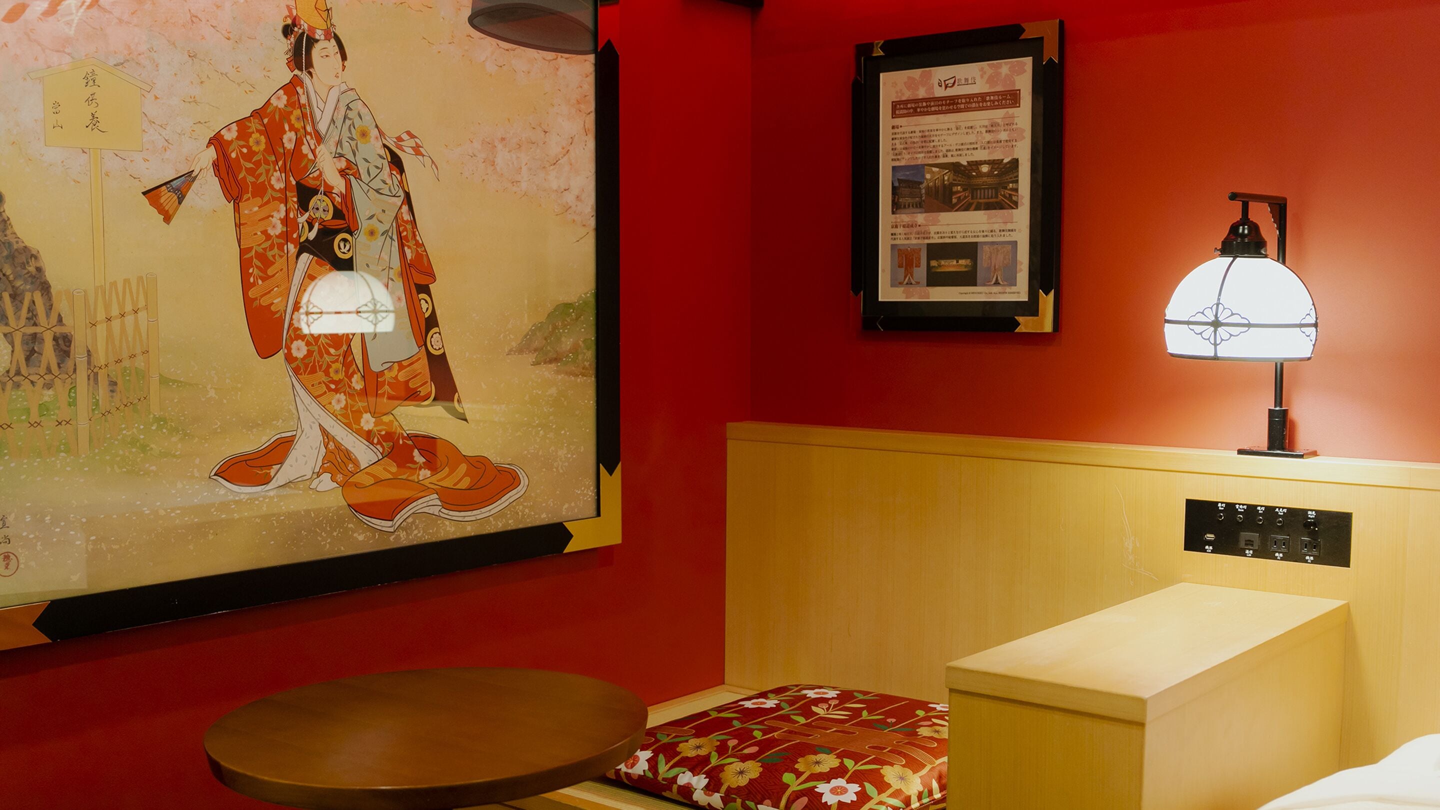 A hotel room with a traditional Japanese painting, a wooden headboard with a lamp, and a small round table.