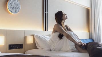 A hotel room with a bed, bedside table, wall-mounted light, and a decorative plate.