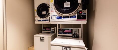 A laundry facility with two dryers and two washing machines, each with Japanese instructions and a coin-operated interface.