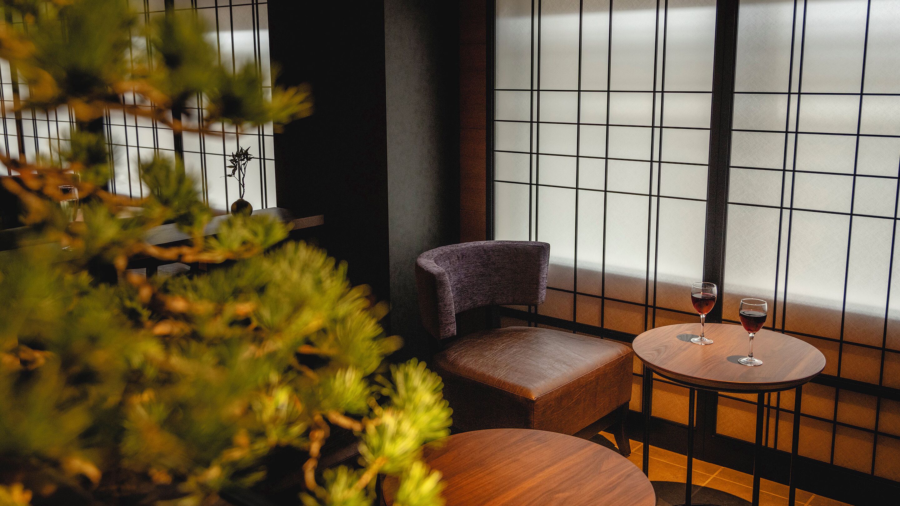 A cozy seating area with a cushioned bench and a small round table, a glass of red wine, and a potted plant.