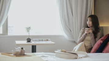 A room with a bed, a small table with a plant, a cup, and a book.