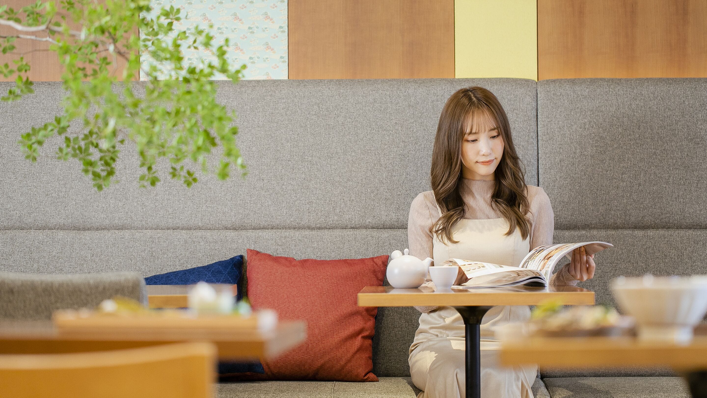 A person sitting on a grey sofa with a table in front, reading a magazine.