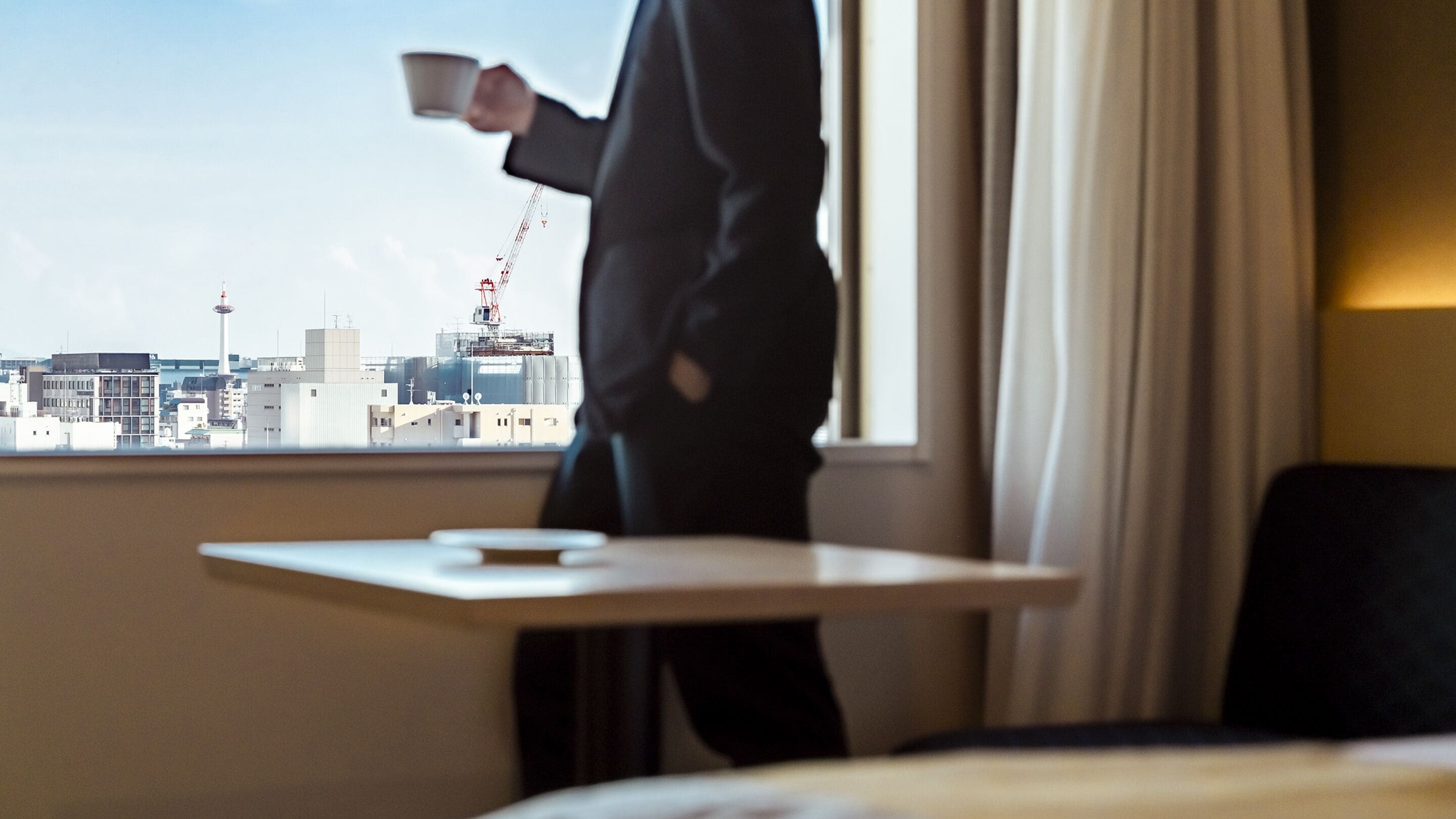 A hotel room with a city view, a table with a cup, and a bed.