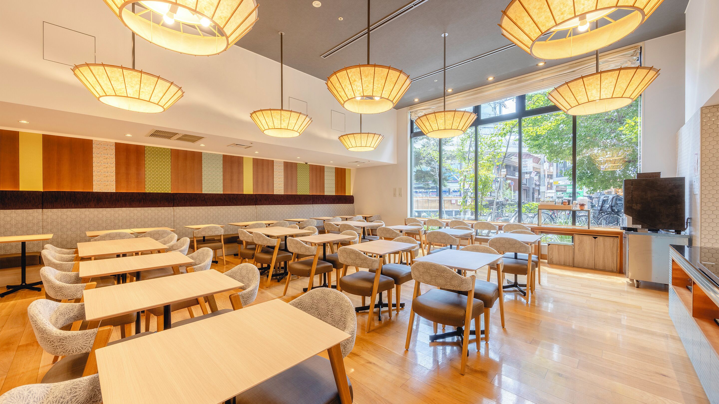 A spacious dining area with multiple tables and chairs, large windows offering a view of the city, and modern pendant lighting.