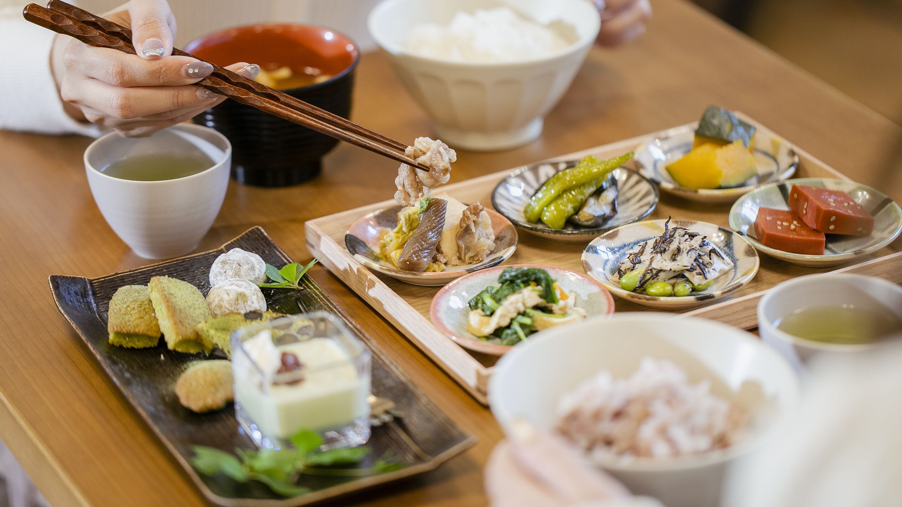 Diverse Japanse gerechten op een houten tafel, waaronder sushi, sashimi en andere traditionele voedingsmiddelen, met stokjes en soepkommen.
