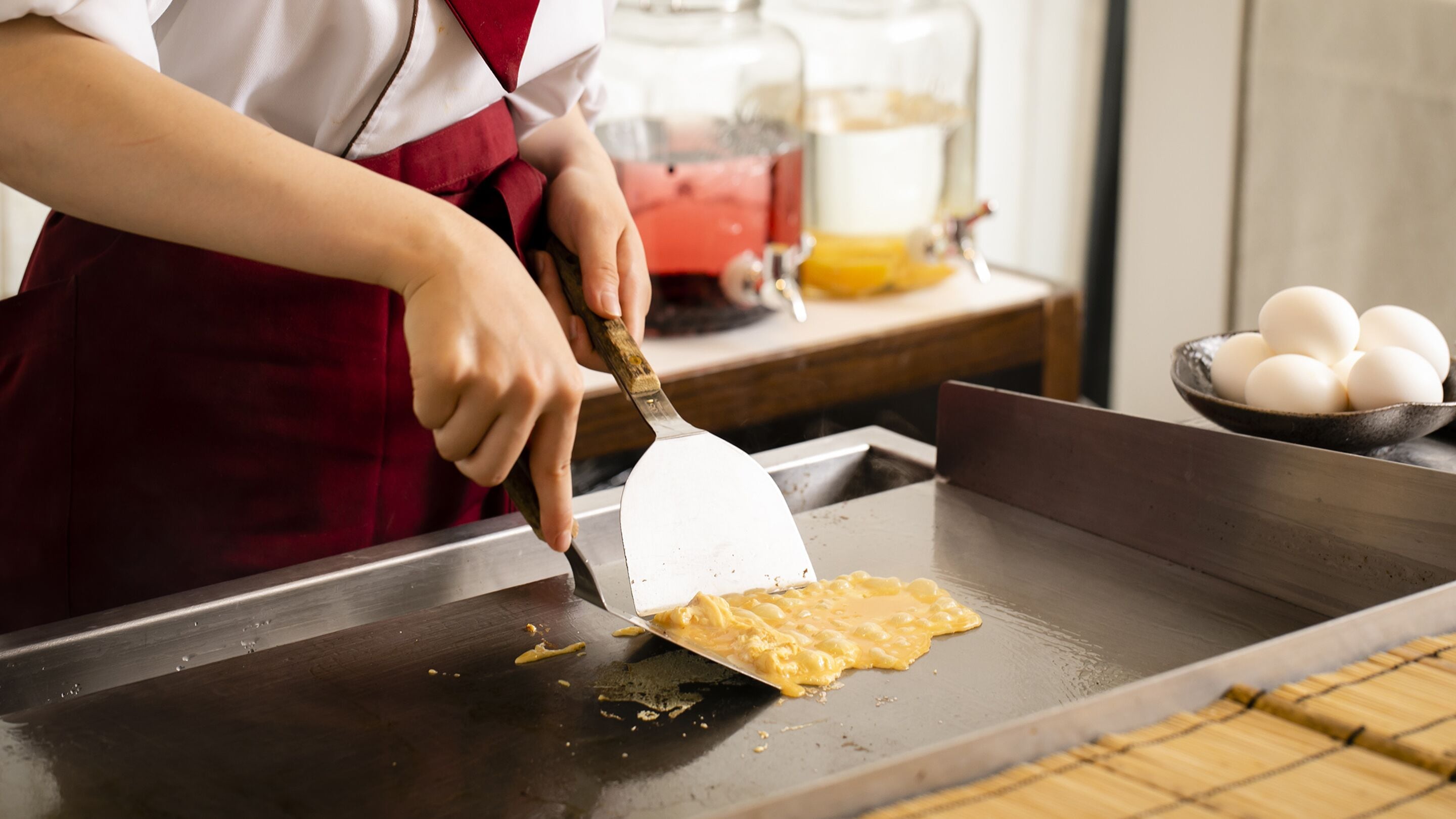 A person cooking on a griddle, with a bowl of eggs and a carton of milk in the background.