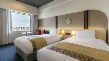 Habitación de hotel con dos camas, vista a la ciudad, un reloj de pared redondo y una pequeña mesa con una taza y un platillo.