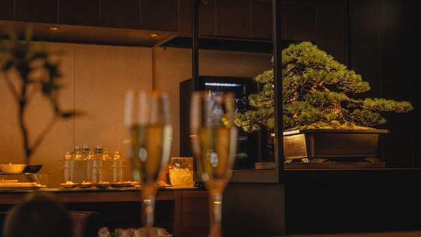A dining area with a bonsai tree, a glass table, and a modern interior design.